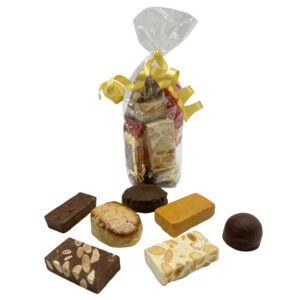 Knuspriger spanischer Turrón in transparenter Geschenkverpackung mit goldener Schleife, umgeben von verschiedenen traditionellen spanischen Süßigkeiten, perfekt für festliche Anlässe.