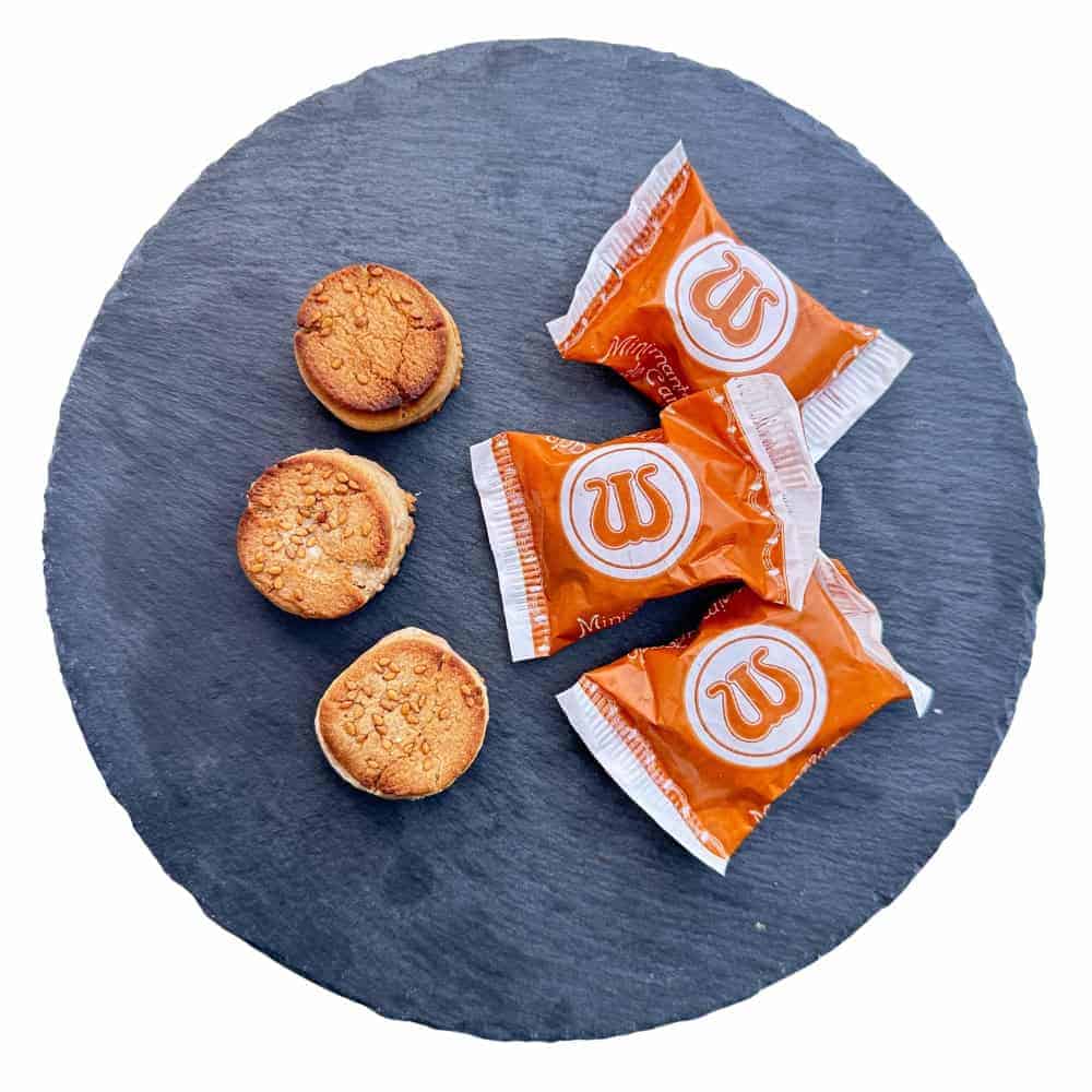 Knusprige spanische Kekse und individuell verpackte Süßwaren auf einer schwarzen Natursteinplatte, typisch für Mareni – Direkt aus Spanien.