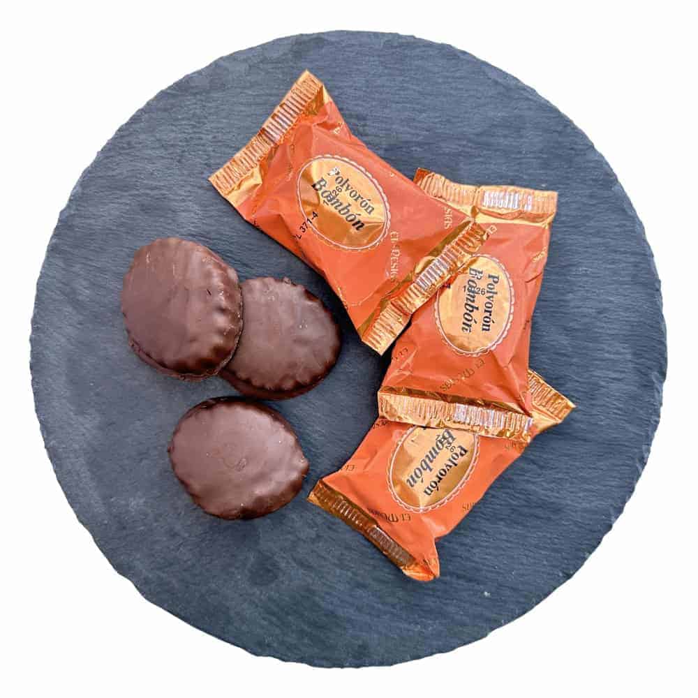 Zwei Schokoladenkekse und zwei einzelne gekaufte Toffees auf einem schwarzen Steinplatten, typisch spanische Süßigkeiten, Mareni – direkt aus Spanien, hochwertige spanische Süßwaren, perfekte spanische Geschenke, süße Leckereien aus Spanien.