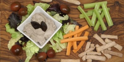 Frischer Dip mit schwarzem Knoblauch, umgeben von Gemüse und Snacks, präsentiert auf Holztablett.