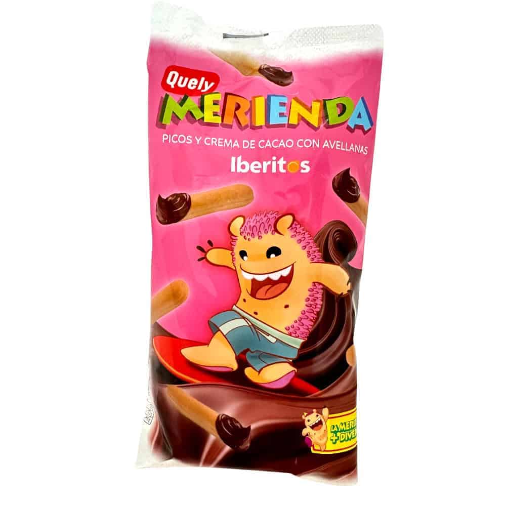 Knallbunte Verpackung der Quely Merienda mit einem fröhlichen, cartoonartigen Monster, das auf einem Surfbrett steht, umgeben von Schokoladen- und Haselnusscreme.