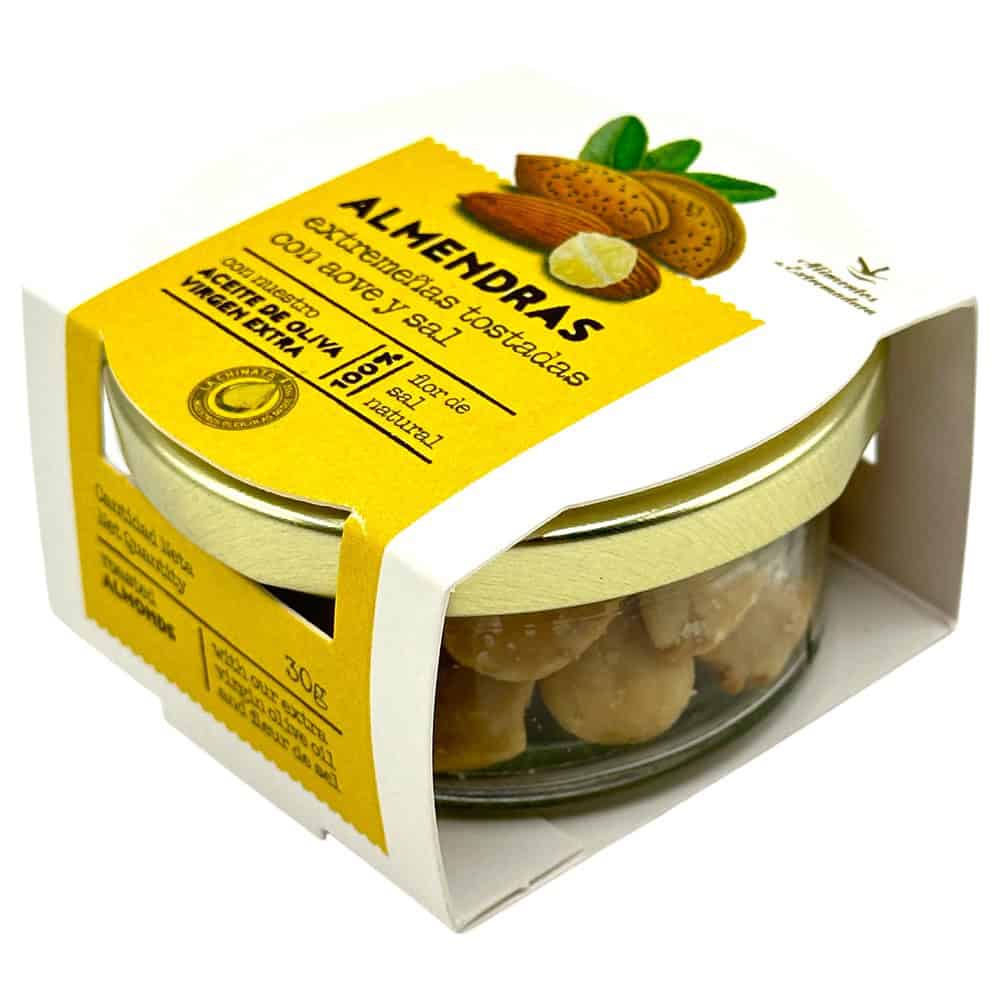 Geröstete Mandeln mit nativem Olivenöl extra und Fleur de Sel in einem Glasbehälter, verpackt in einer weißen Schachtel mit gelbem Etikett.