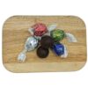 Kokospralinen mit Schokoladenüberzug, serviert auf Holzbrett, farbige Bonbons in der Hintergrundreihenfolge.